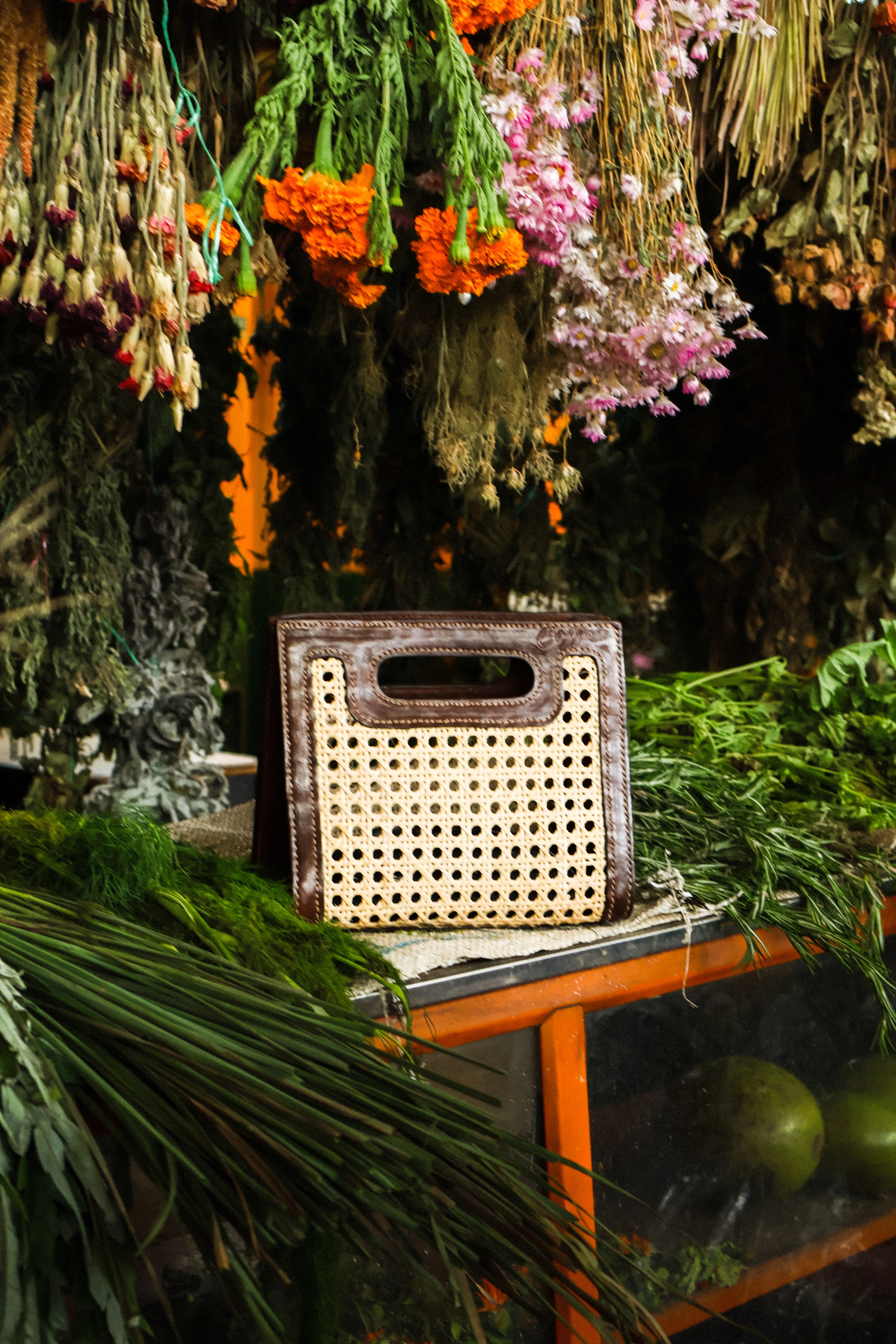 Bolso Coffe Cocoon hecho con hojas de palma iraca marrón natural tejidas a mano rodeadas de plantas y flores